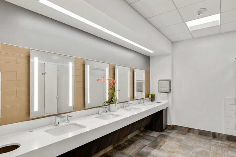 Modern commercial bathroom with sleek sinks and illuminated mirrors, crafted by LAY Construction.