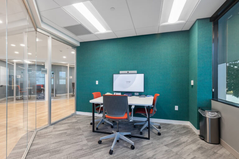 Modern office meeting room with glass walls, ergonomic chairs, and a large wall-mounted screen for professional collaboration.