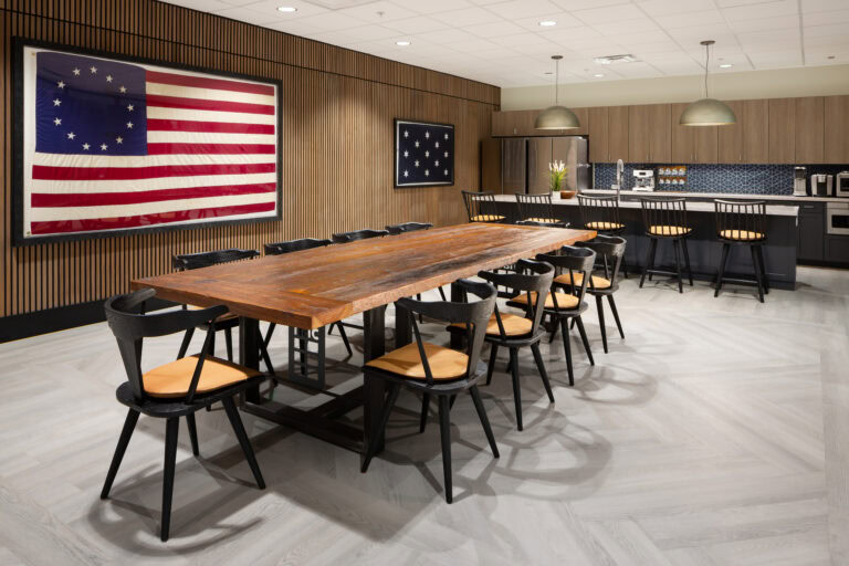 Modern office kitchen and conference space with American flag wall art, wooden accents, and stylish furnishings.