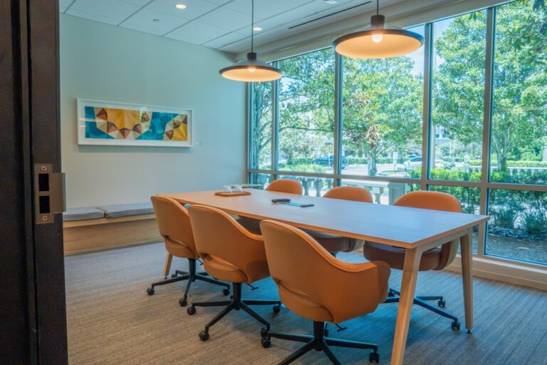 Modern conference room with large windows and orange chairs around a wooden table.