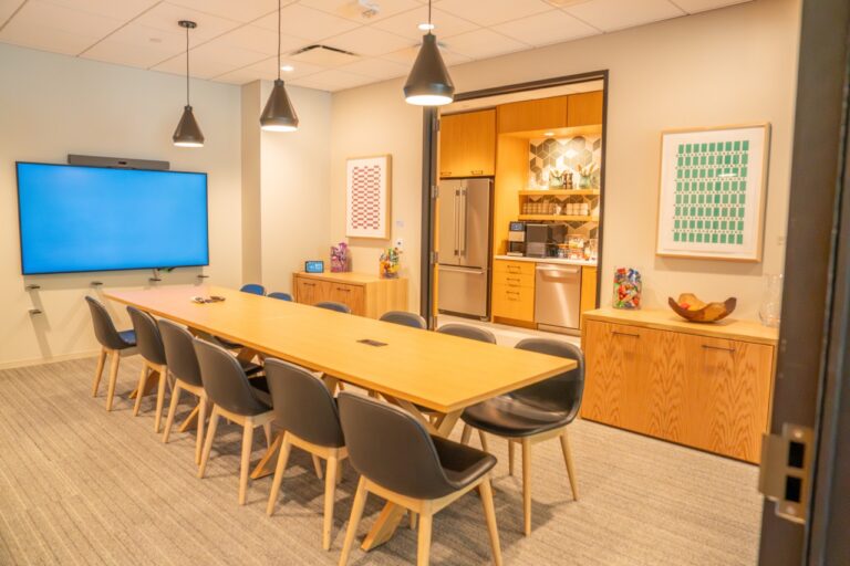 Modern conference room with a large wooden table and black chairs.