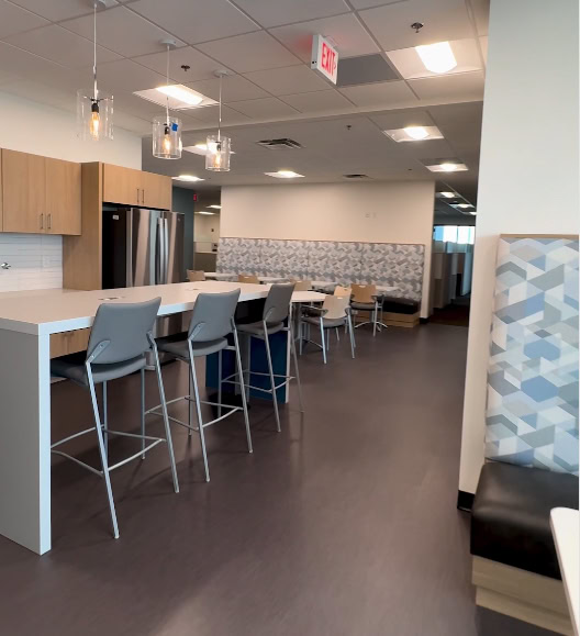 Modern office break room with seating and kitchen area.
